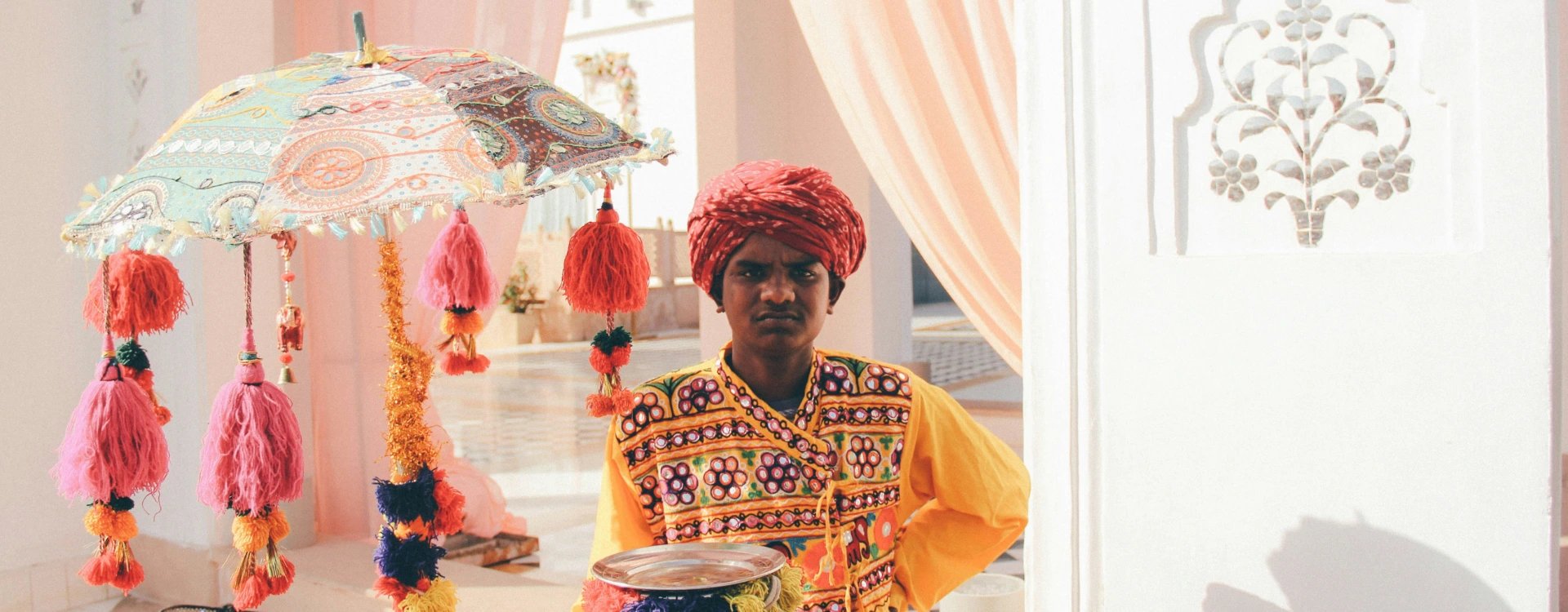 image of man wearing a turban and traditional attire carrying a plate with an ornate umbrella in background