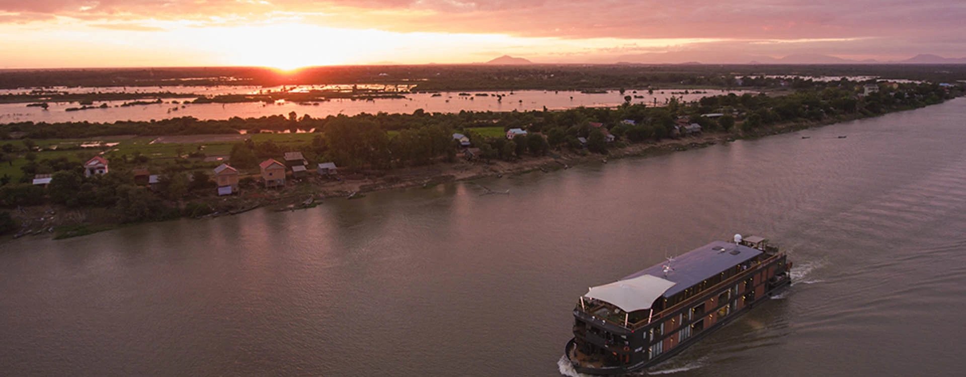 The Aqua Mekong sailing along the Mekong River at sunset.