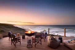 Table and chairs around a firepit at sunset at Lekkerwater Beach Lodge