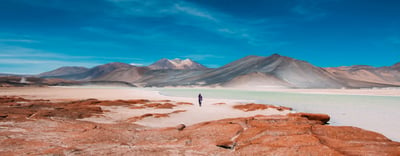 a person walking across a desert plain with mountains in the background