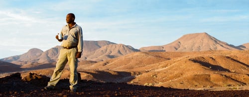 Man standing in foreground with red dunes of Namibia in background